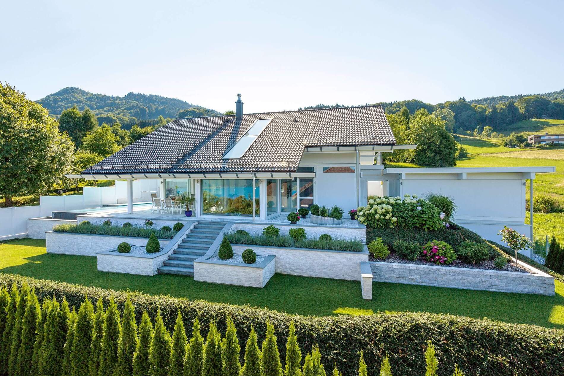 Modernes Haus mit Aussicht auf Hügel und See, umgeben von Garten.