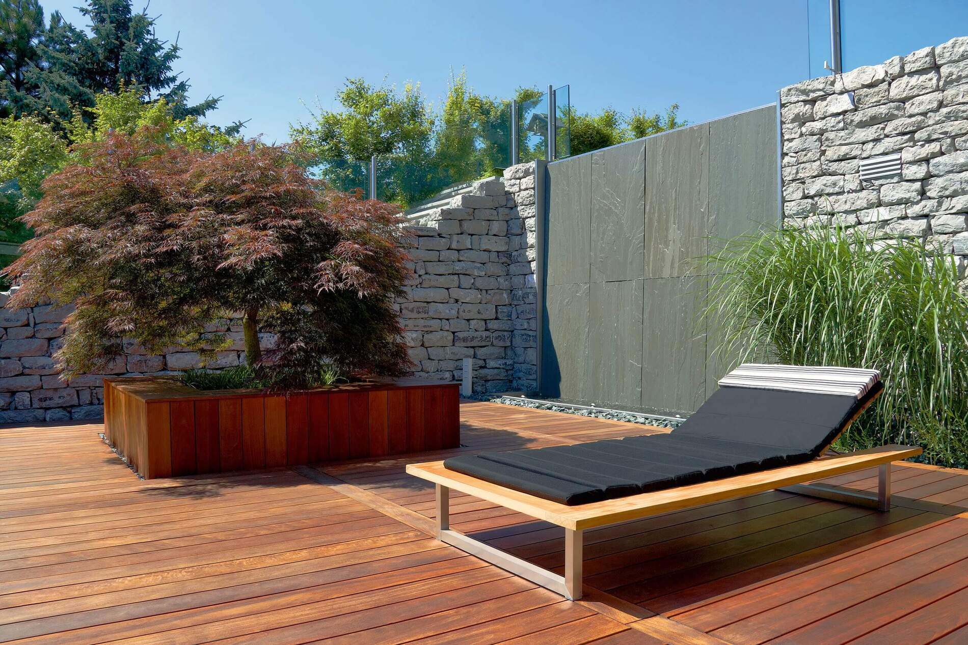 Elegante Liege auf einer Holzterrasse mit bepflanzten Akzenten