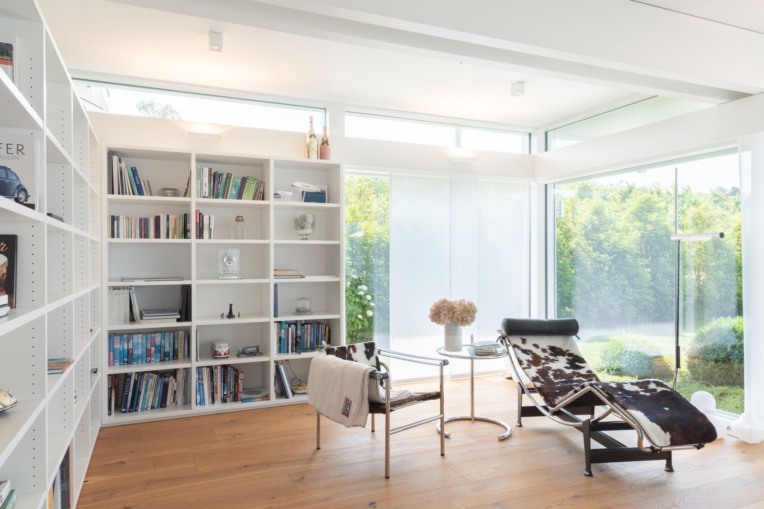 Helles Wohnzimmer mit großem Fenster, Bücherregal und relaxender Liege