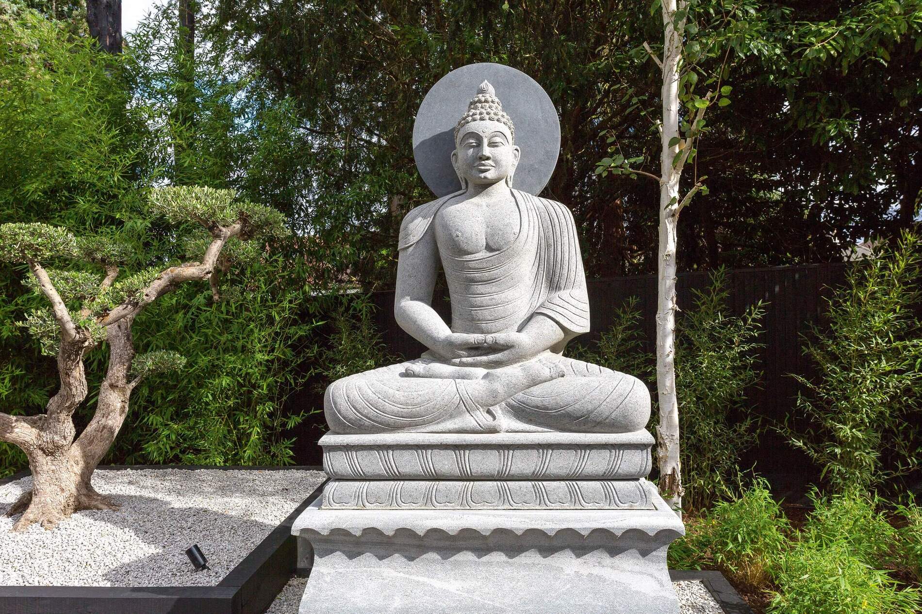 Graue Buddha-Statue im Garten mit Pflanzen und Kies