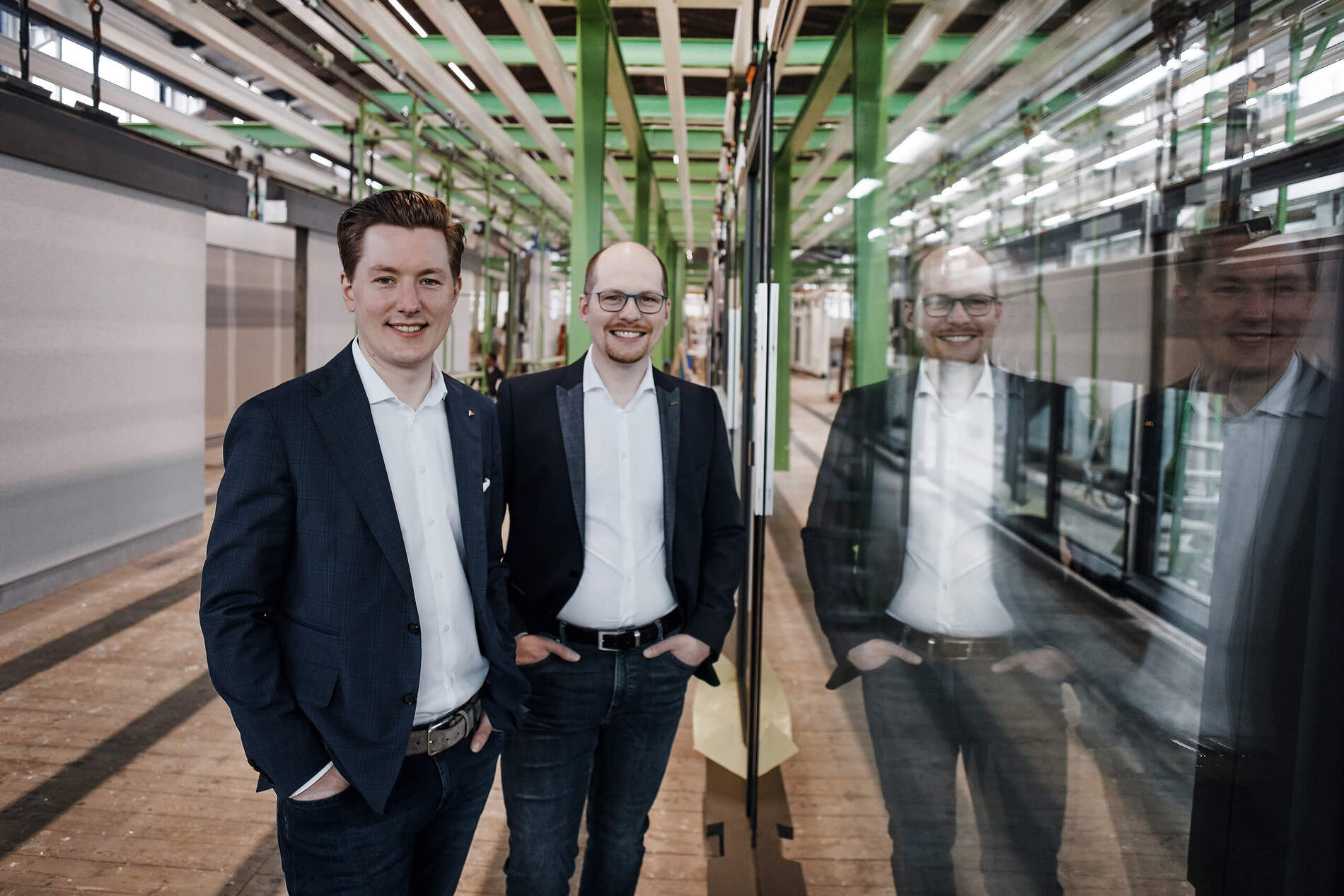 Zwei Männer in moderner Industrieumgebung Zwei Männer posieren vor einem gläsernen Element in einer Fabrikhalle