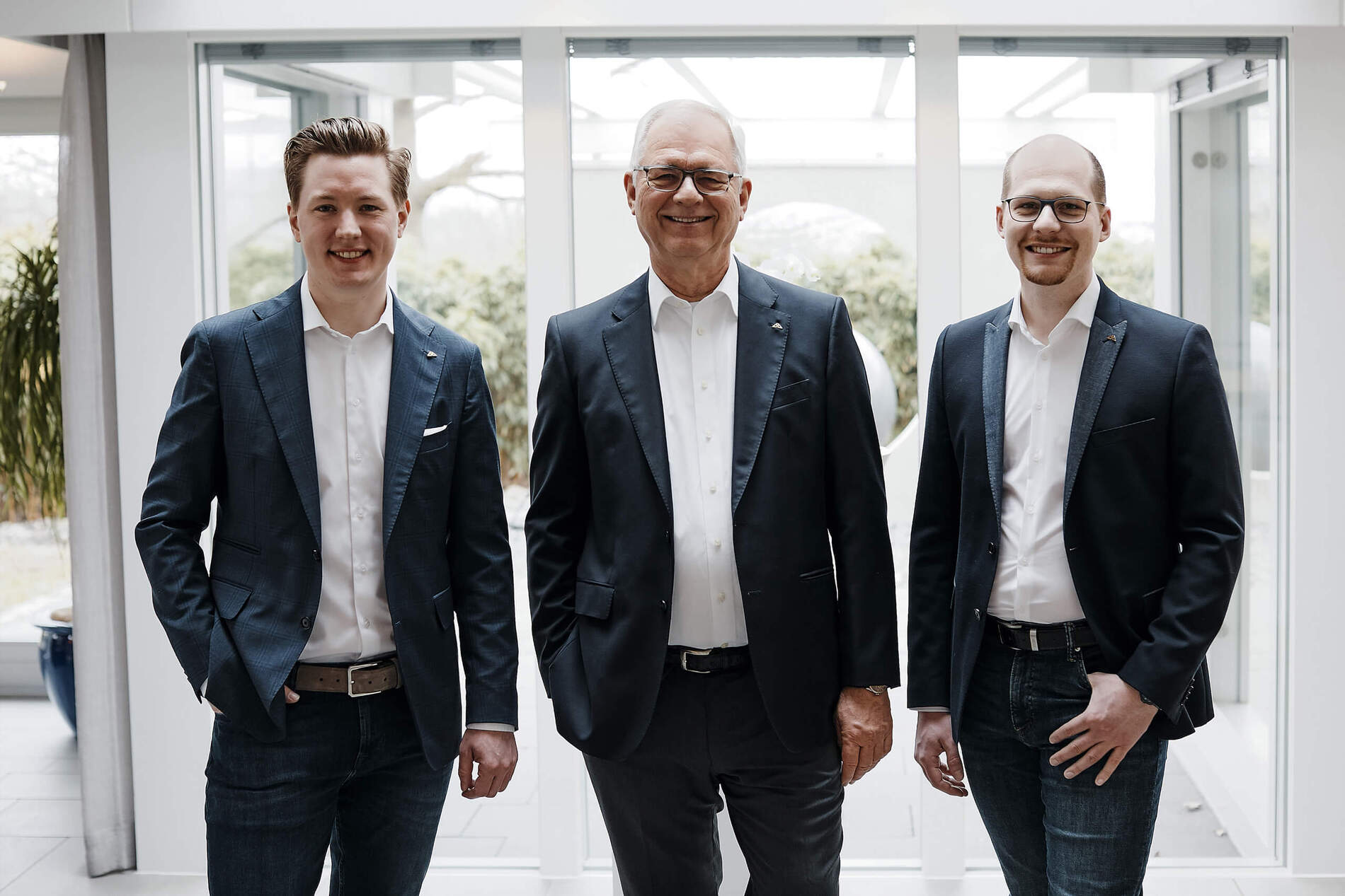 Drei Personen in Anzügen vor Glasfenstern Drei Männer posieren für ein Foto in einem modernen Bürogebäude