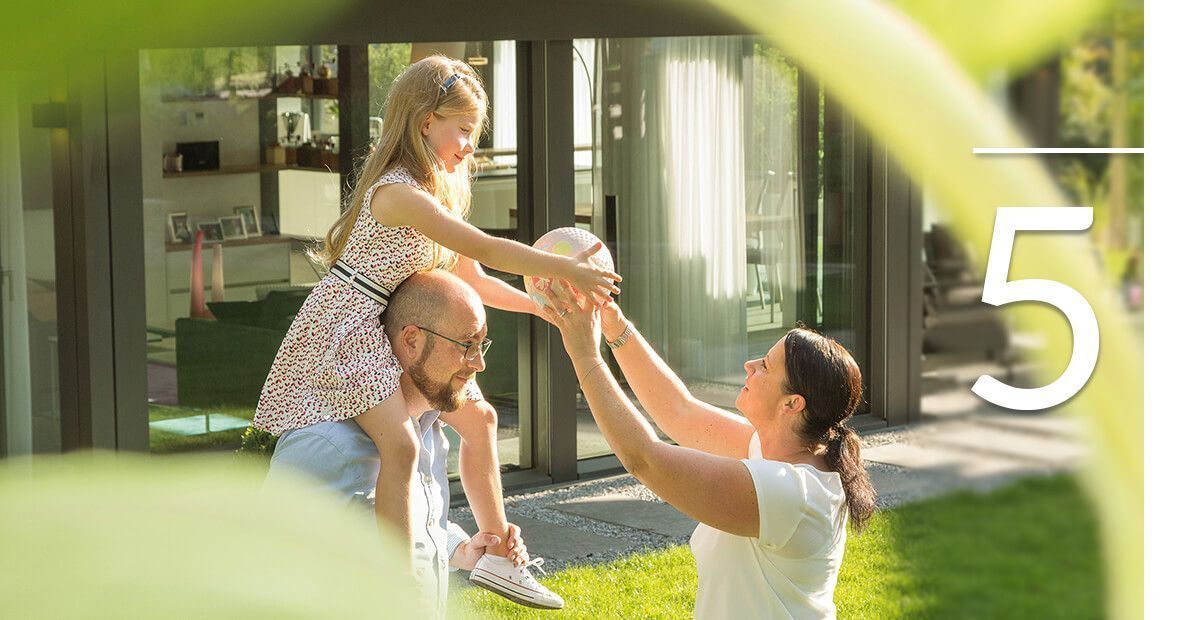 Familienaktivität im Freien mit Kind Ein Mann hebt ein Kind hoch, während eine Frau zuschaut und lacht.