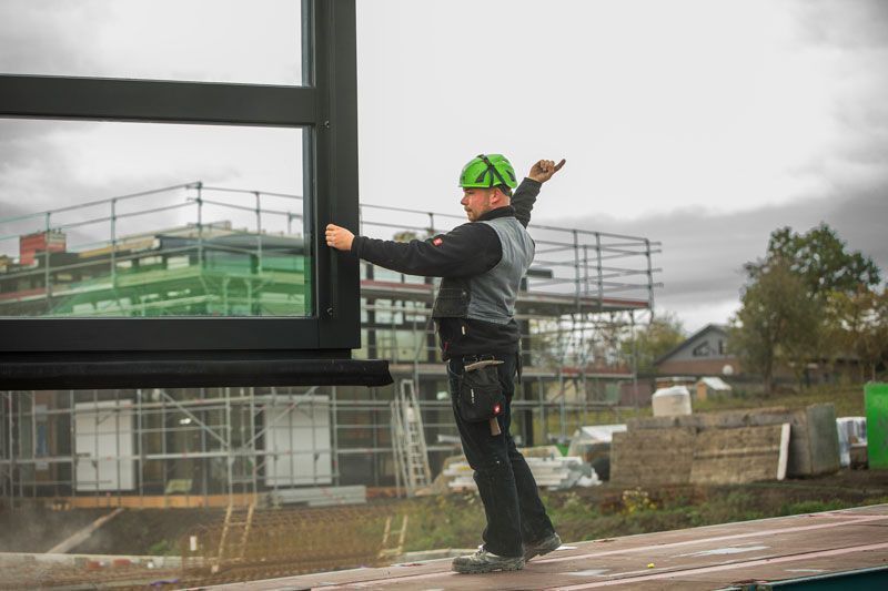 Arbeiter bei der Montage eines großen Fensters Handwerker in Sicherheitshelm installiert Fenster auf Baustelle