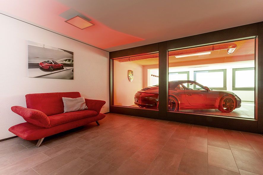 Elegantes Interieur mit Sportwagen in Glasbox Moderne Raumgestaltung mit rotem Sofa und Porsche im Hintergrund