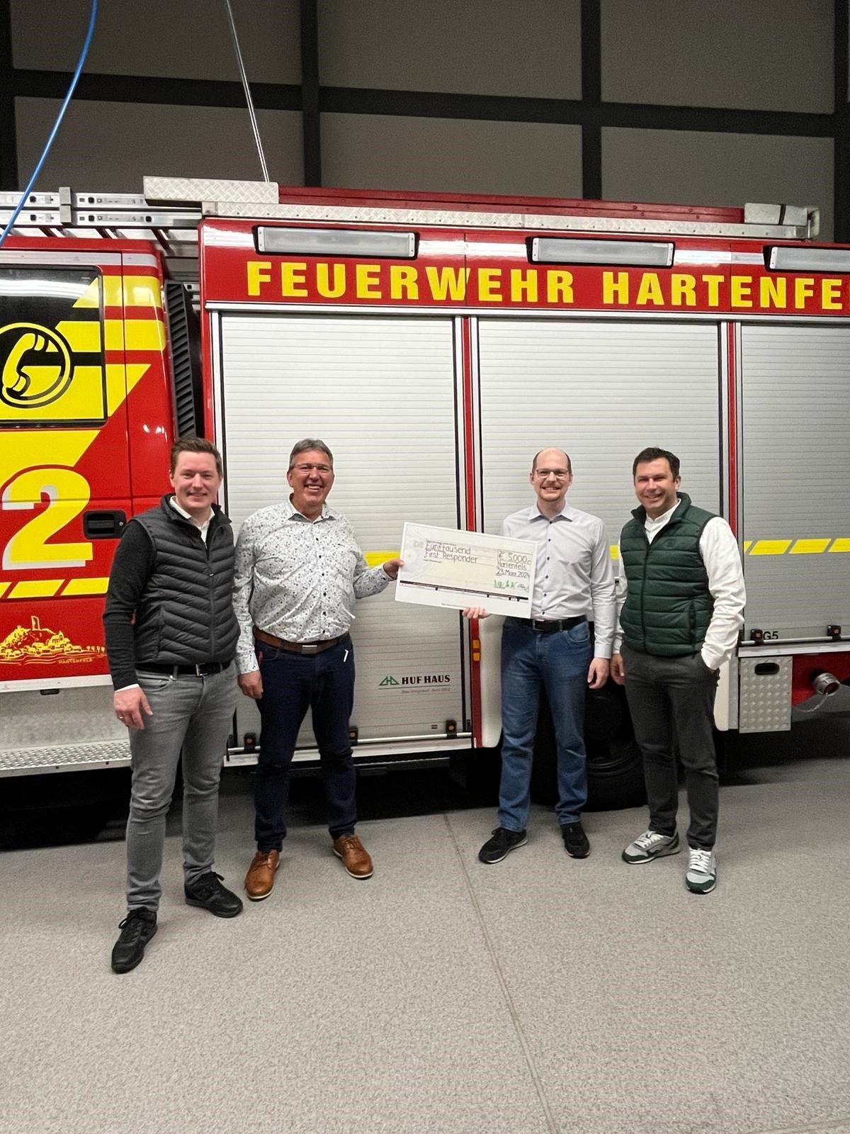 Übergabe eines Schecks an die Feuerwehr Hartenfels Vier Personen stehen vor einem Feuerwehrauto und halten einen Scheck.
