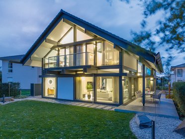 Einfamilienhaus mit Glasfassade und Garten bei Nachtbeleuchtung