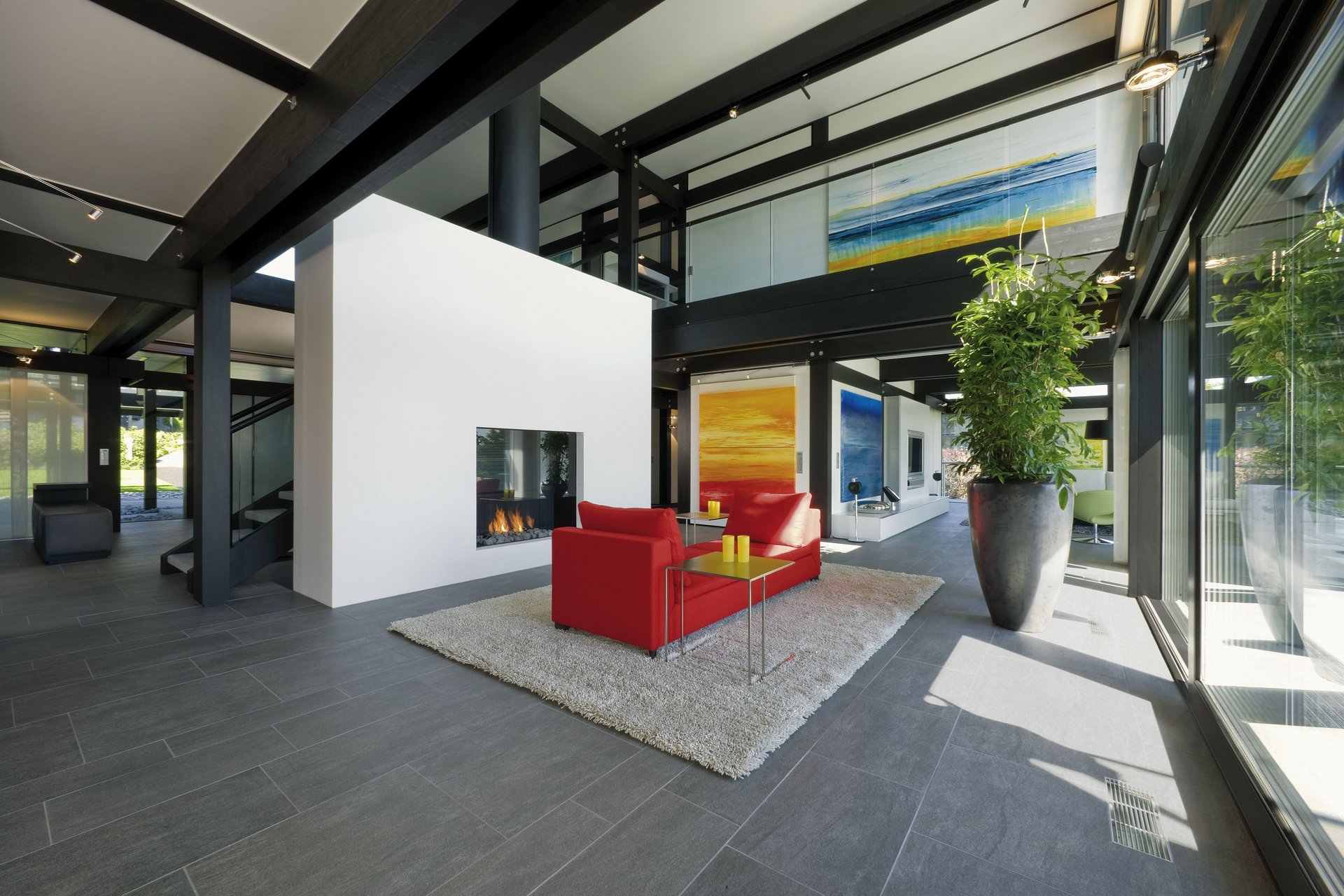 Modernes Wohnzimmer mit rotem Sofa und Kamin Helles, modernes Wohnzimmer mit großflächigen Fenstern und Kunstwerken