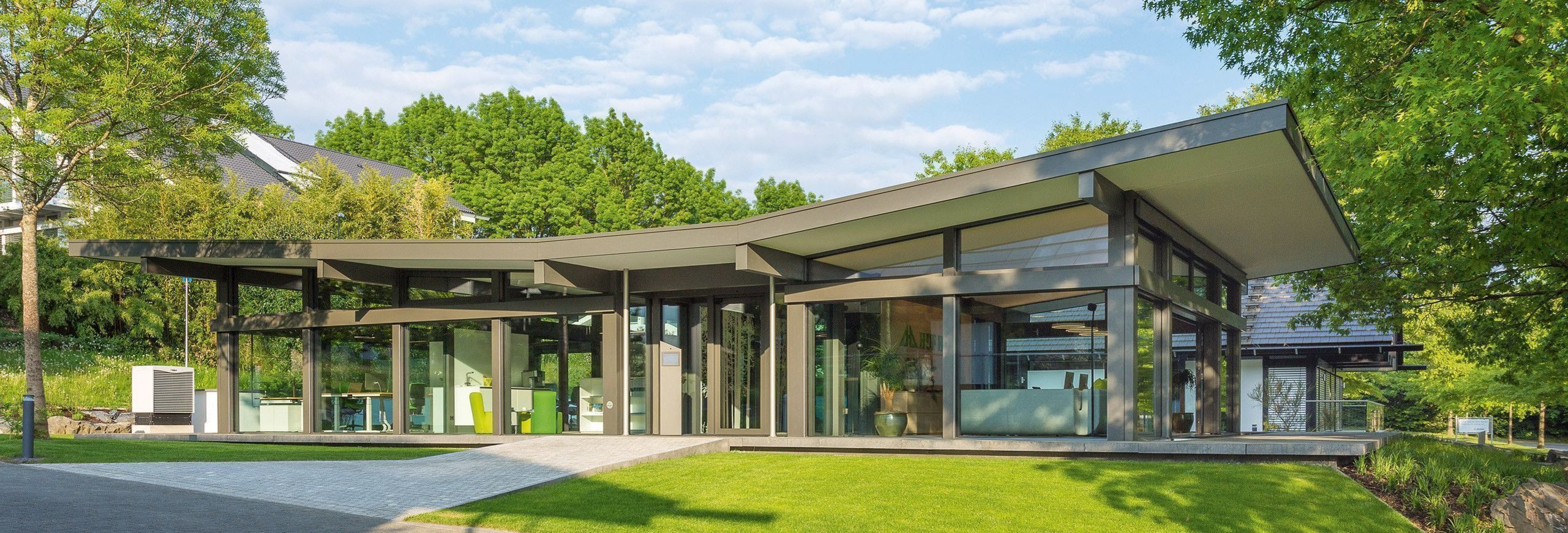 Moderne Architektur mit geschwungenem Dach und Glasfronten Helles, elegantes Haus umgeben von grünem Garten und Bäumen