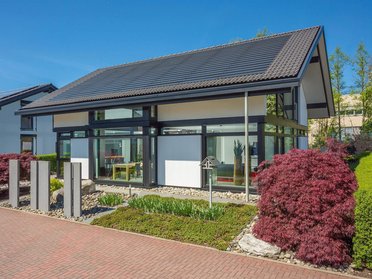 Helles Haus mit großen Fenstern, umgeben von buntem Garten