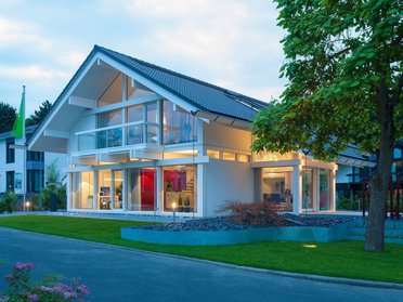 Ein modernes Haus mit großen Fenstern und einem gepflegten Garten bei Dämmerung