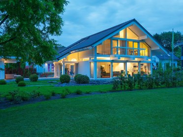 HUF Musterhaus Frankfurt weiss 10 Architektur eines modernen Hauses mit grüner Landschaft und Dämmerungslicht