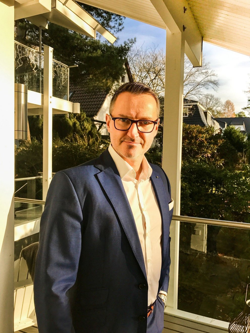 Mann in Anzug auf Balkon im Sonnenlicht Eleganter Mann posiert auf einem Balkon mit Aussicht