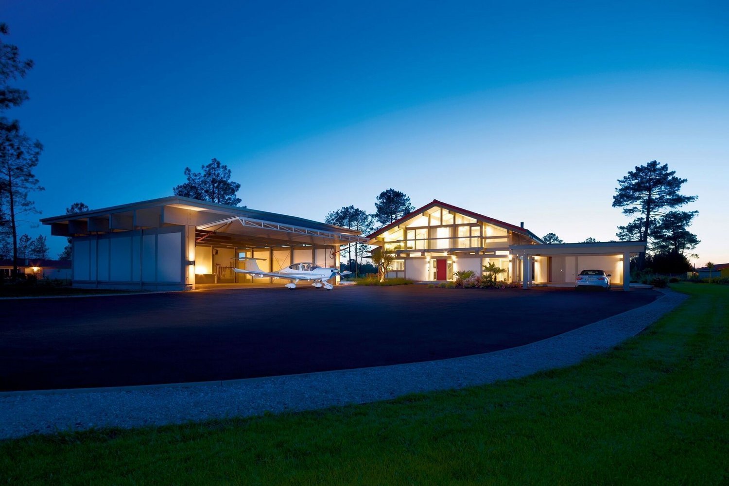 Moderne HUF Haus mit Flugzeughangar bei Nacht HUF Haus mit integriertem Flugzeughangar und sanfter Beleuchtung