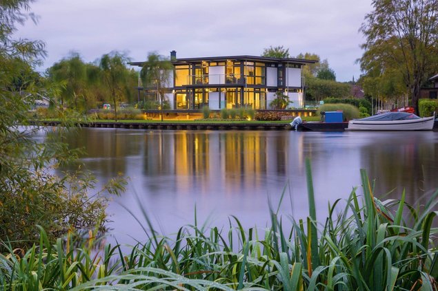 Luxushaus mit Flachdach am Wasser Modernes Haus mit Flachdach und Wasseransicht, umgeben von Pflanzen