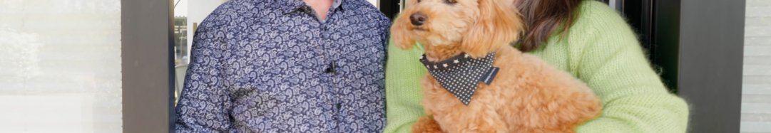 Ein Mann und eine Frau stehen vor einer Eingangstür mit einem Hund.