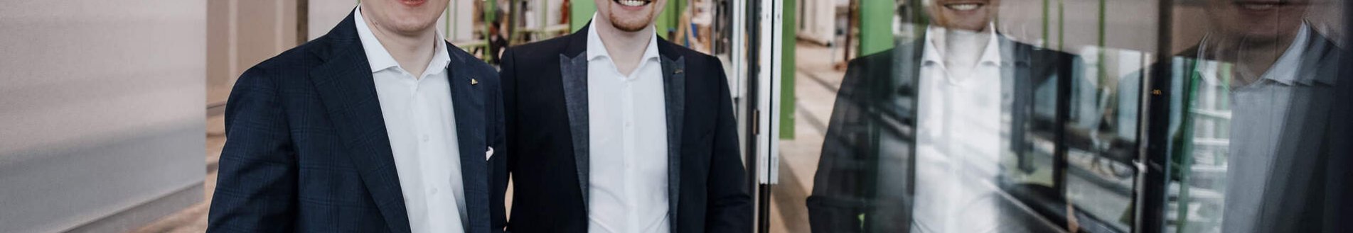 Zwei Männer posieren vor einem gläsernen Element in einer Fabrikhalle