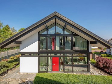 Haus mit gewinkeltem Dach, großen Fenstern und gepflegtem Garten