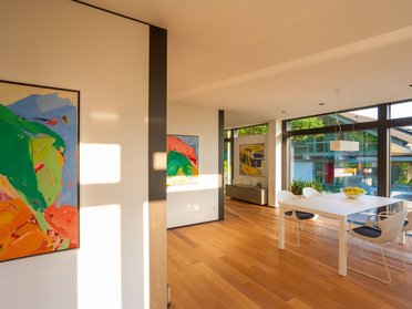 Modum7 10 Innenansicht 9 Helles Wohnzimmer mit großen Fenstern, modernen Möbeln und bunten Gemälden