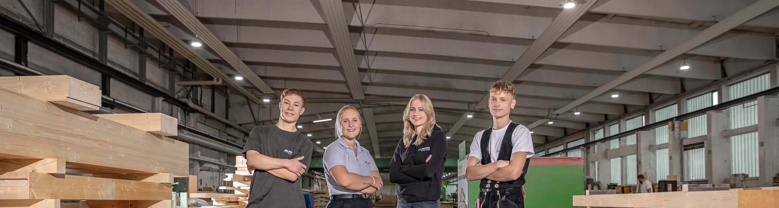 Mitglieder eines Teams in einer Holzfabrik Vierte Personen stehen in einer Holzfabrik zwischen Holzstämmen