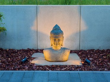 Stilvolle Buddha-Skulptur im Gartenbeleuchtung Gemütliche Buddha-Skulptur aus Stein in einem japanischen Garten
