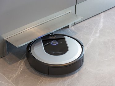 Ein Roboterstaubsauger ruht unter einer Küchenzeile auf einem modernen Boden