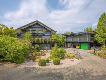 Modernes HUF Haus mit Dreifach-Garage und Bürogebäude Ansicht eines modernen HUF Hauses mit Garage und Büro, umgeben von Grün