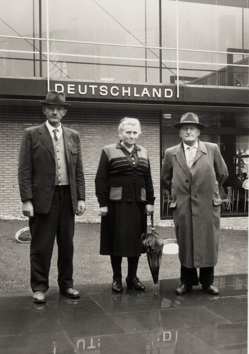 Historisches Foto einer Gruppe vor Gebäude Deutschland Drei Personen in formeller Kleidung vor einem Gebäude mit dem Schriftzug Deutschland