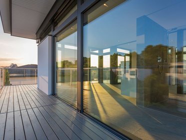 Moderne HUF Aufstockung eines Bestandshauses Terrasse mit Glasfront und Blick auf die Stadt bei Sonnenuntergang