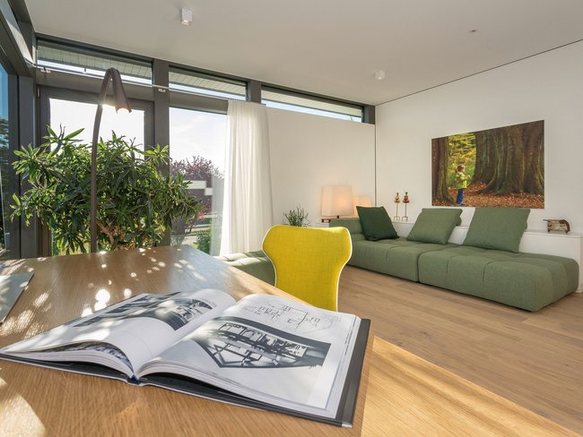 Ein heller Raum mit Sofa, Tisch und großen Fenstern.