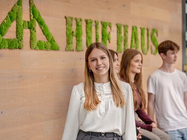 Junge Erwachsene vor Huf Haus Wand Lächelnde Frau mit langer blonder Haar neben drei weiteren Personen