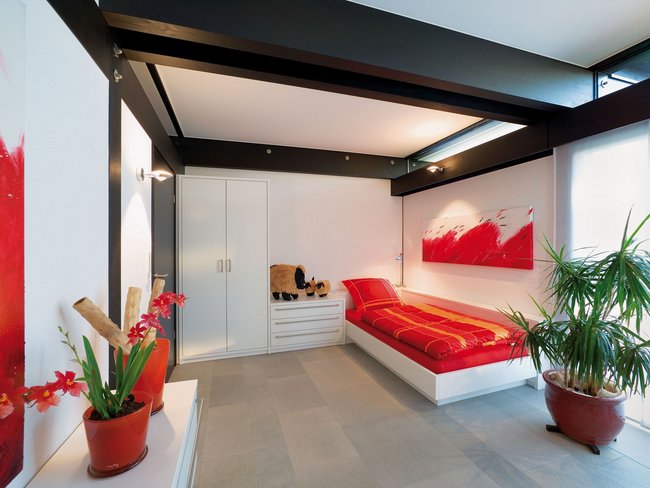 A contemporary bedroom featuring a red bedspread and decorative plants