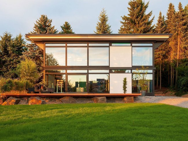 HUF modum Flachdach ebenholz 2 Ein modernes Fachwerkhaus mit Flachdach und großen Fenstern in einer grünen Umgebung.