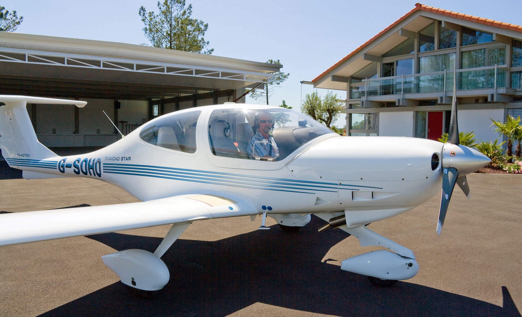 HUF Haus mit Flugzeughangar und Propellerflugzeug Flugzeug vor modernem Haus und Hangar, sonniger Tag