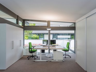 Helles Büro mit grünen Stühlen und großen Fenstern
