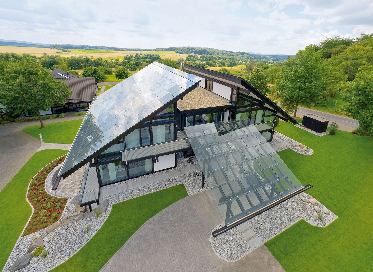 HUF Dorf Musterhauszentrum ART 9 3 Ein modernes Gebäude mit Glasdach und großem Garten in ländlicher Umgebung.