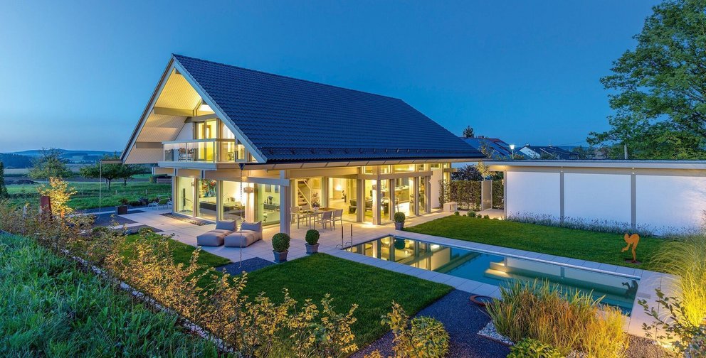 Stilvolles Haus mit beleuchtetem Garten und gläserner Fassade bei Dämmerung