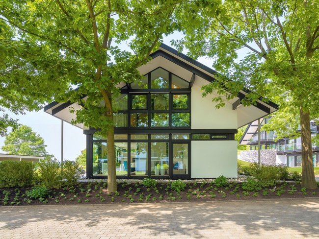 Modum7 10 Aussenansicht 1 Ein modernes Gebäude mit großen Fenstern, umgeben von Bäumen und Grünflächen.