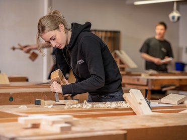 Junge Frau beim Holzarbeiten in einer Werkstatt Eine Frau arbeitet konzentriert mit einem Meißel an Holz in einer Tischlerei