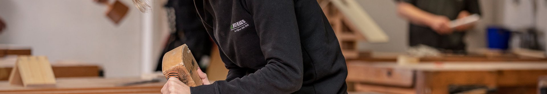 Eine Frau arbeitet konzentriert mit einem Meißel an Holz in einer Tischlerei