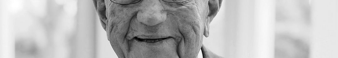 Elderly man smiling, wearing glasses and formal attire