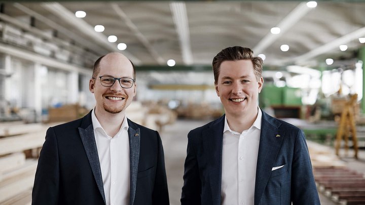 Zwei Männer stehen in einer Holzwerkstatt Freundliche Männer in Anzügen vor Holzregalen in einer Werkstatt