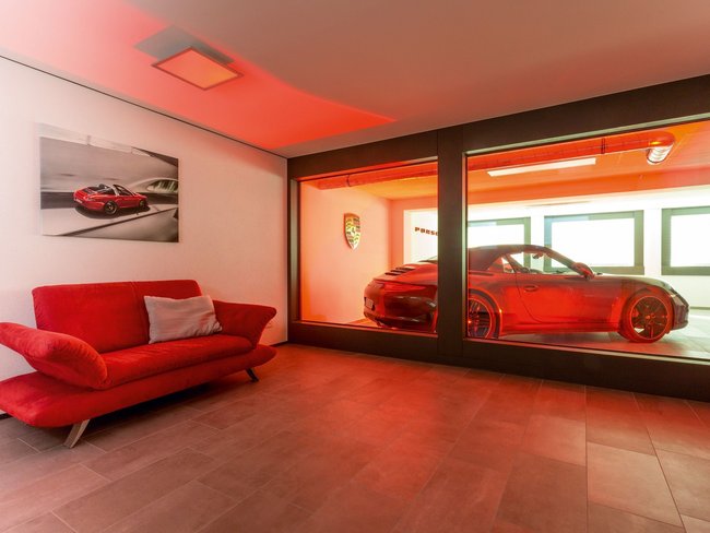 Bungalow mit rotem Sofa und Porsche in der Glasbox