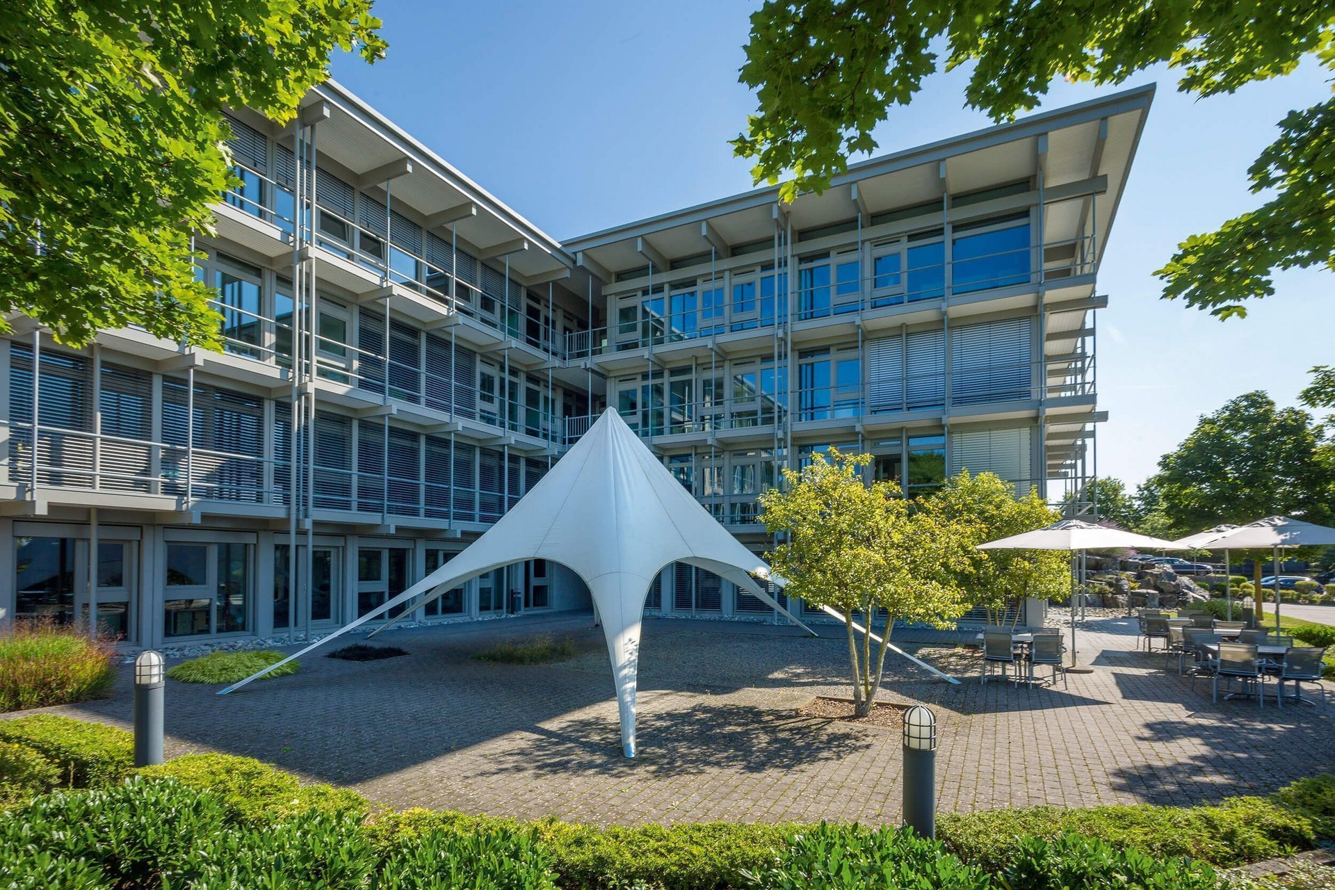 Moderne Bürogebäude mit Sonnensegel und Grünflächen Bürogebäude HUF mit Sonnensegel und Pflanzen im Vordergrund