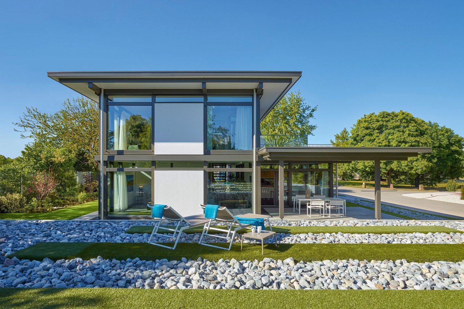 Moderne Architektur mit Glas und grünem Raum Ein stilvolles, modernes Haus umgeben von Garten und Steinen