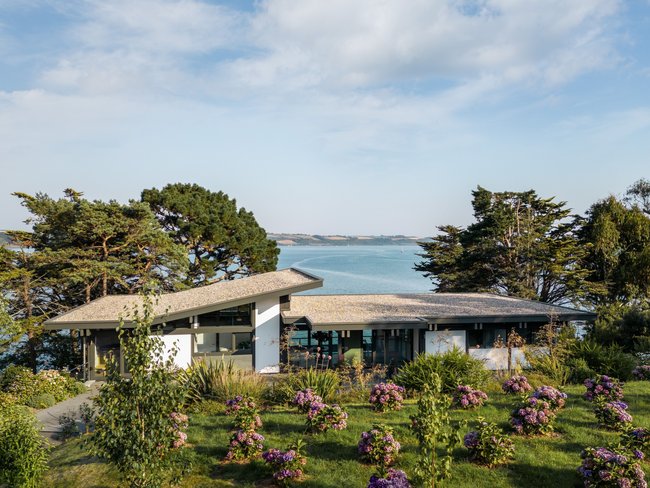 Fachwerkhaus umgeben von Blumen und Bäumen mit Blick auf das Wasser