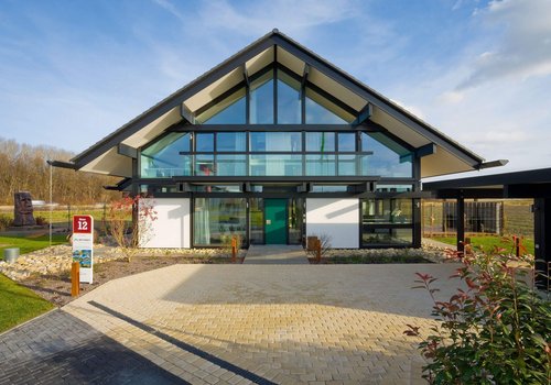 HUF Musterhaus Koeln Fertighauswelt 2 Frontansicht eines modernen Gebäudes mit grüner Eingangstür und Landschaftsgestaltung