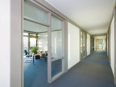 Modernes Bürogebäude mit durchsichtigen Trennwänden Blick auf einen Flur mit Büros und natürlichem Licht