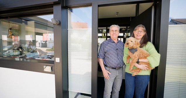 Paar mit Hund vor einem modernen Gebäude Ein Mann und eine Frau stehen mit einem Hund vor der Tür eines modernen Hauses.